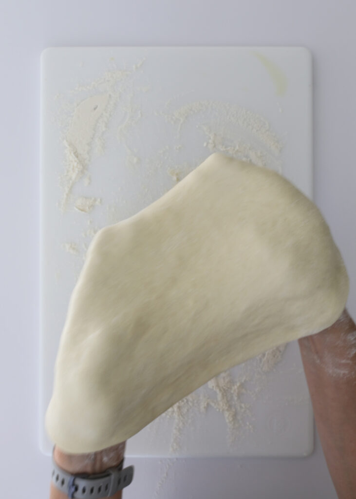 stretching dough between hands above the cutting board.