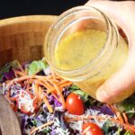 closeup of hand holding jar of lemon dressing to pour into salad.