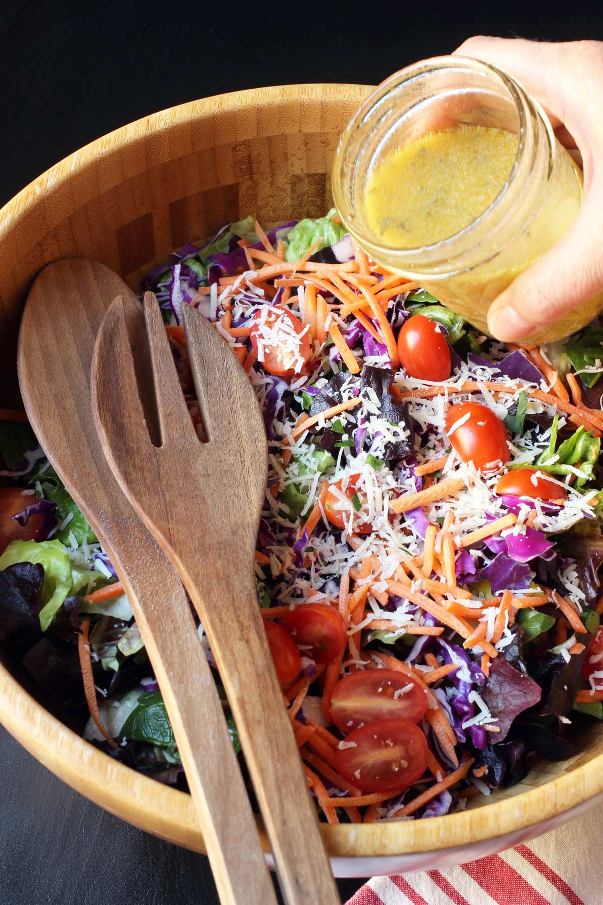 pouring lemon dressing onto green salad in wooden bowl.