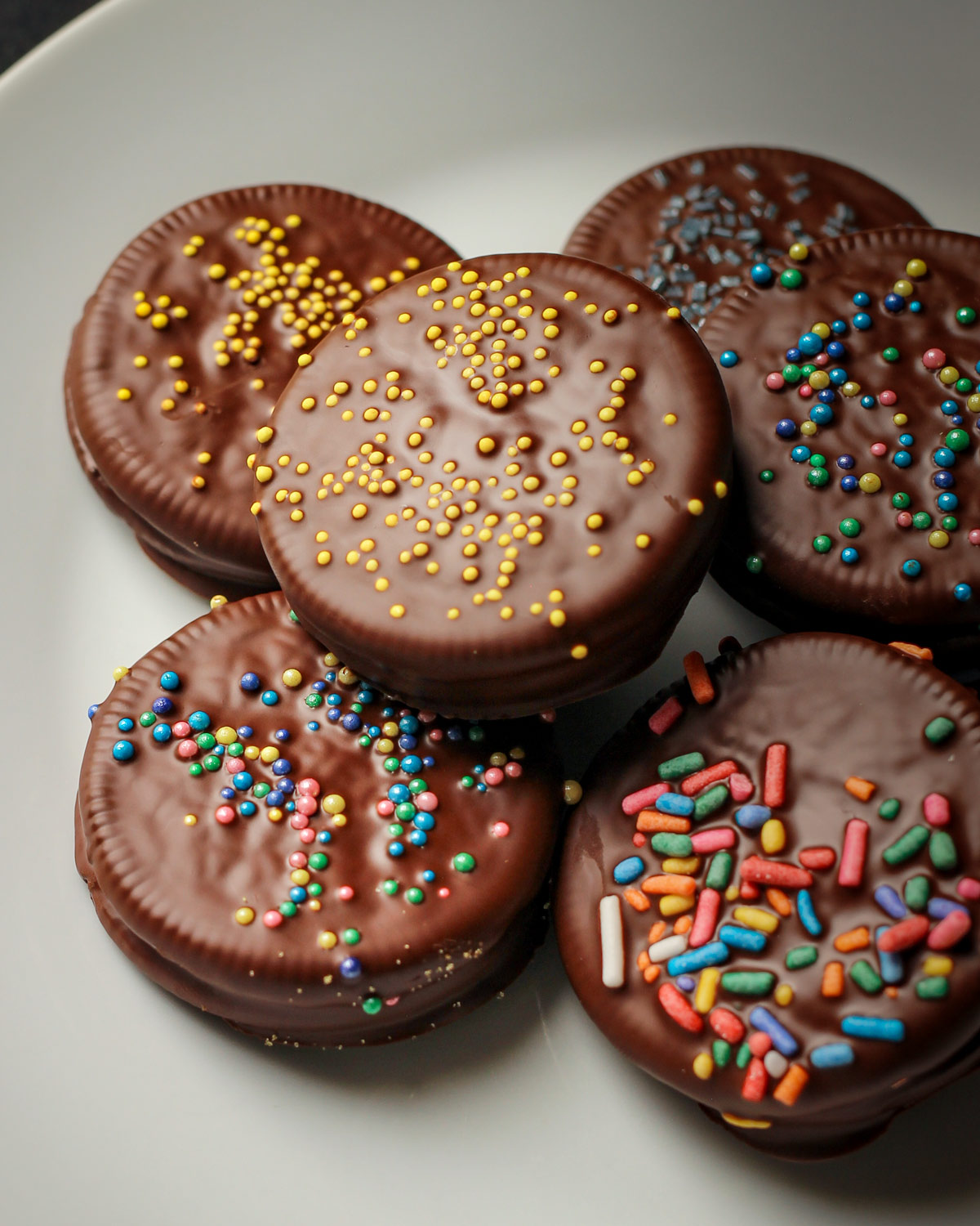 chocolate dipped oreos with colored sprinkles on a white plate.