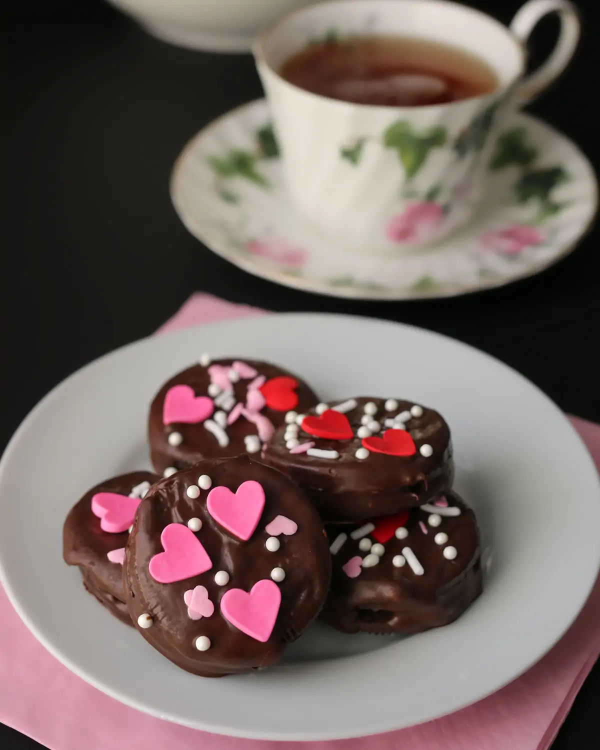 valentine chocolate dipped oreos on a white plate with a pink napkin and a teacup.