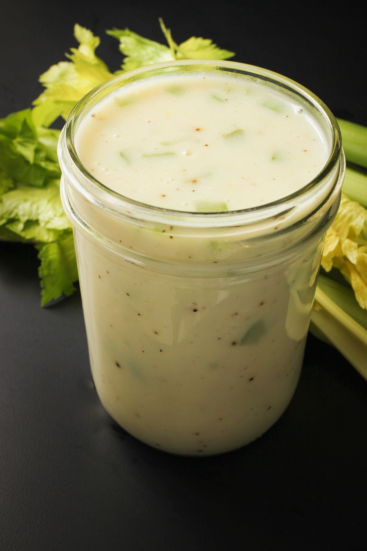 overhead view of a mason jar full of cream of celery soup next to leafy ribs of celery.