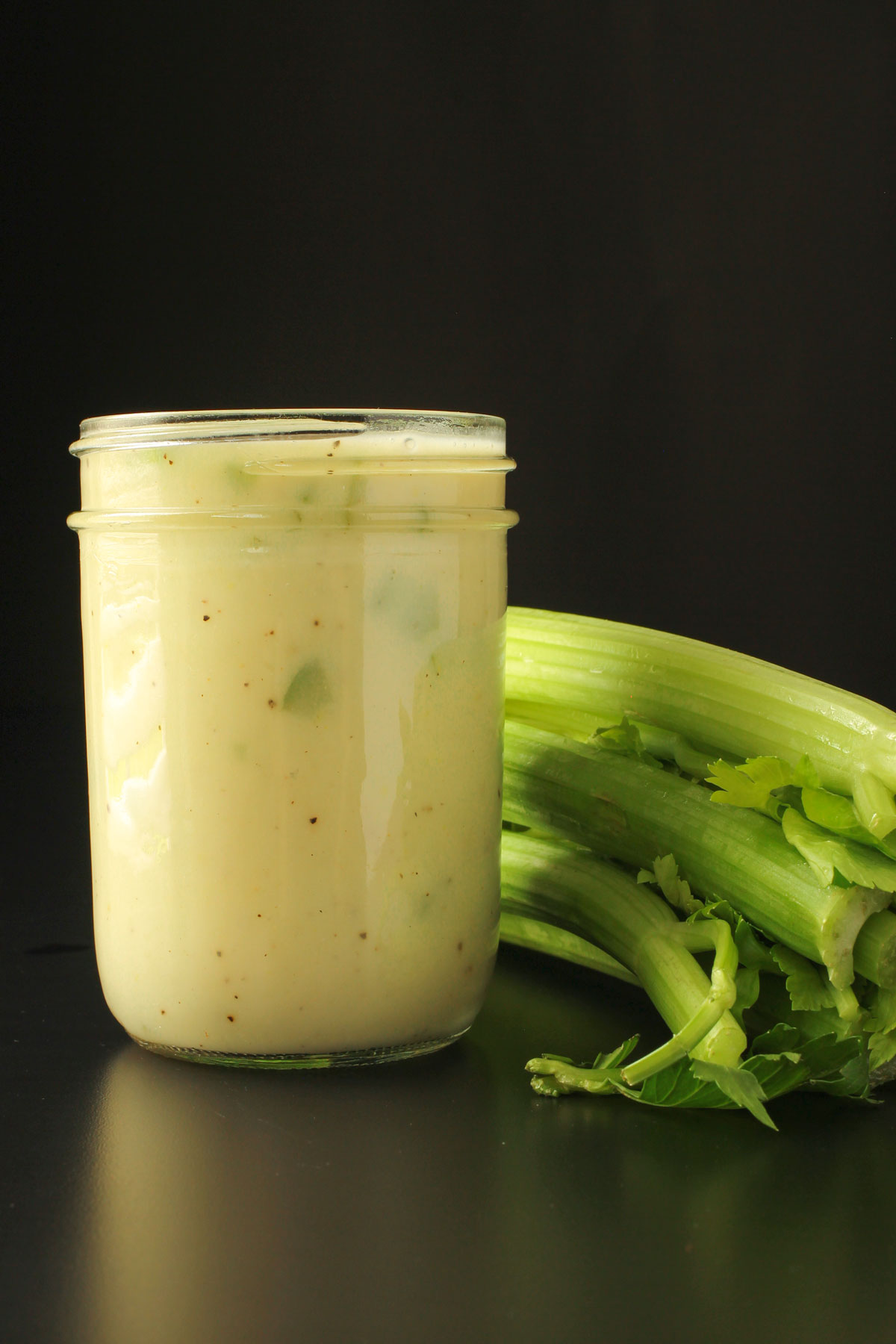 wide-mouth mason jar full of cream of celery soup next to stalk of celery on black table top.