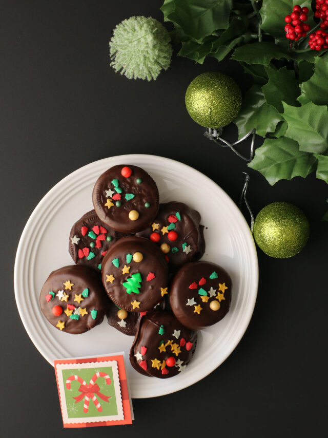 plate of chocolate dipped oreos with a christmas tag, ornaments, and holly on table nearby.