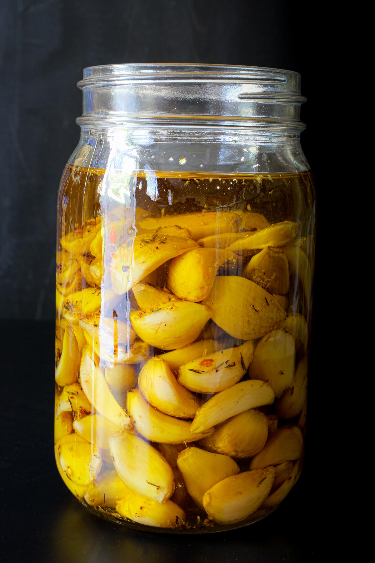 open jar of roasted garlic cloves steeping in olive oil and herbs.