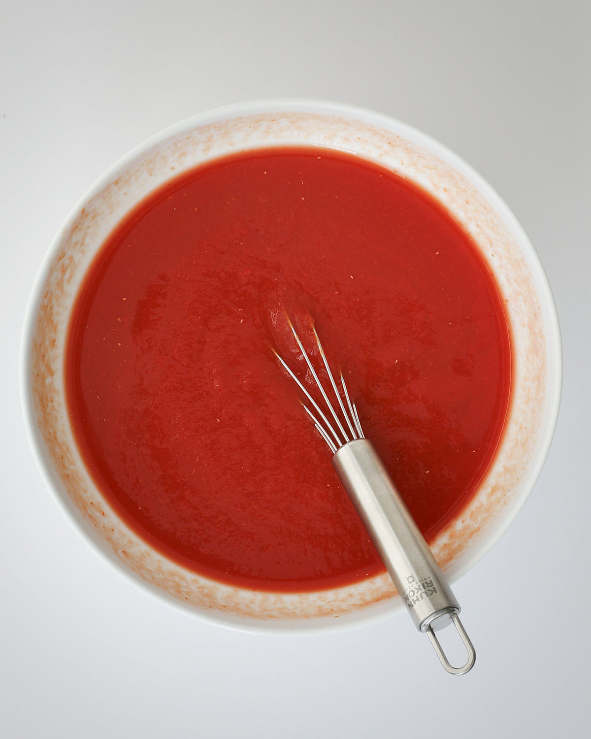 water and tomato paste whisked together in a white bowl.