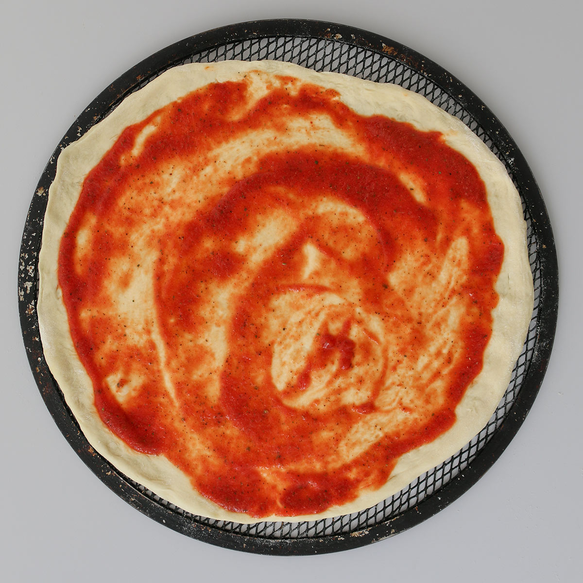round of pizza dough spread with pizza sauce.