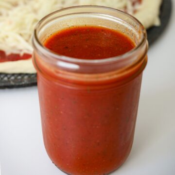 pizza sauce in a jar next to a formed pizza.