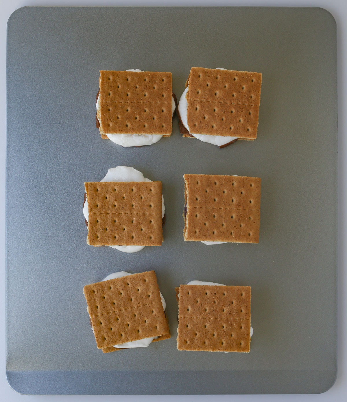 top graham cracker is smooshed down on each smore on baking sheet.