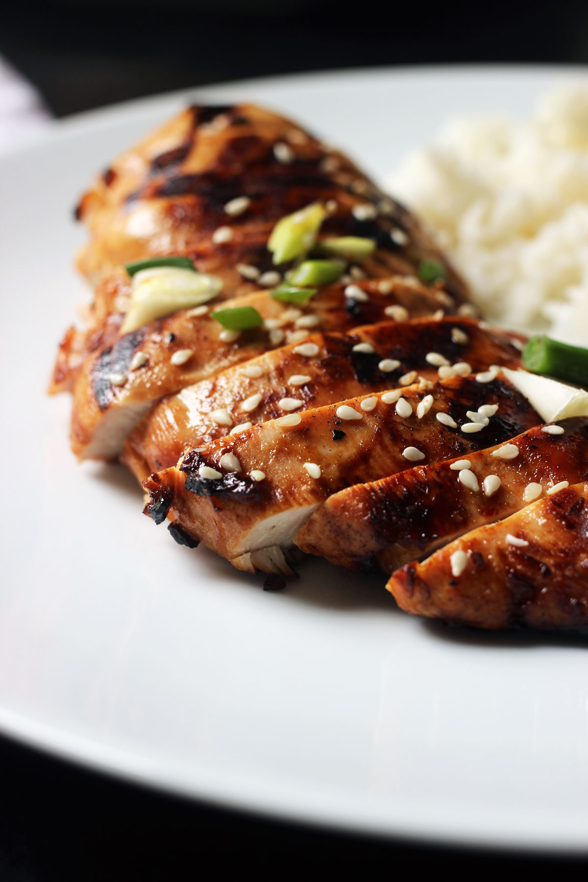 sliced asian chicken breast fanned on a white plate with rice.