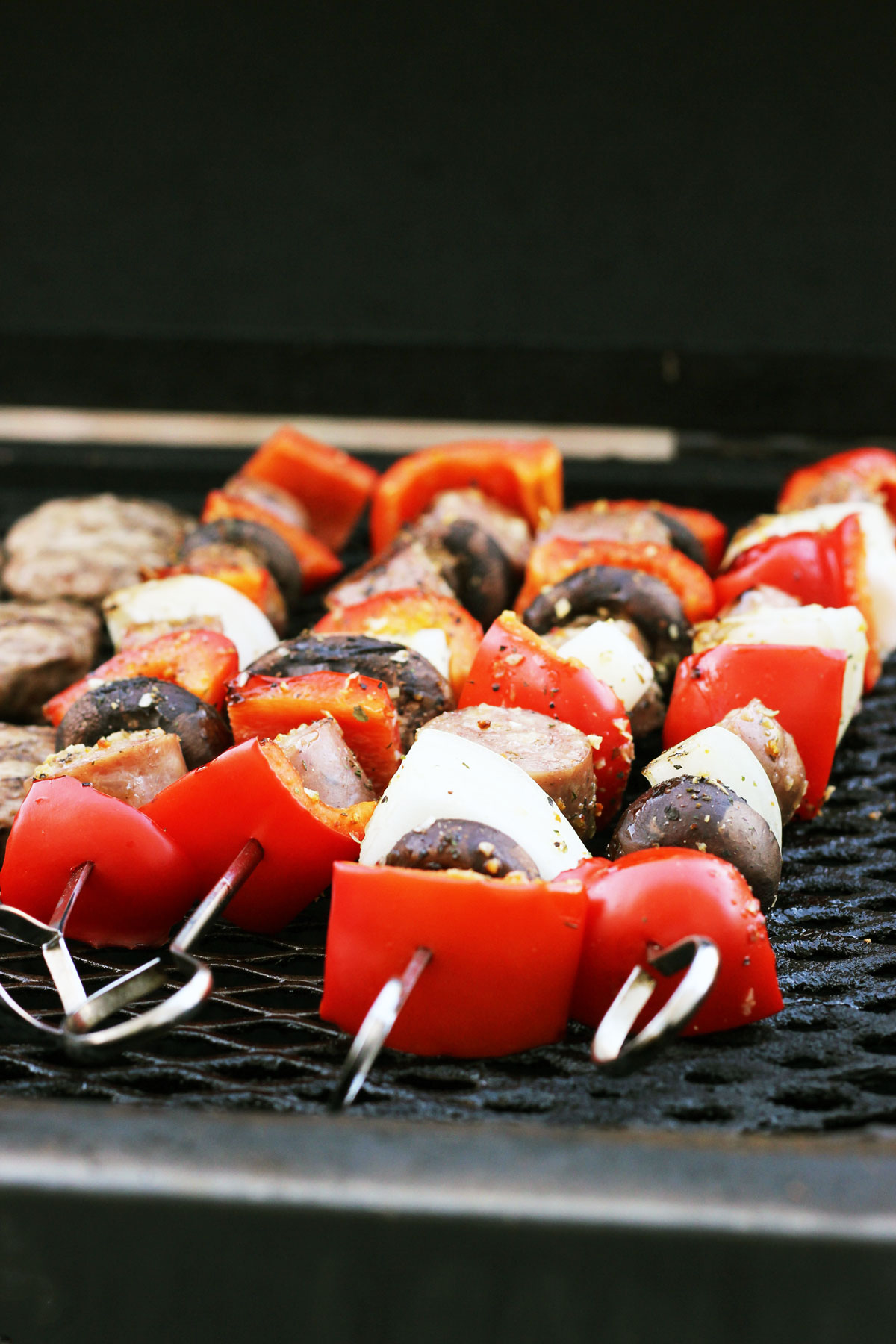 sausage, peppers, and onions on metal skewers on the grill.