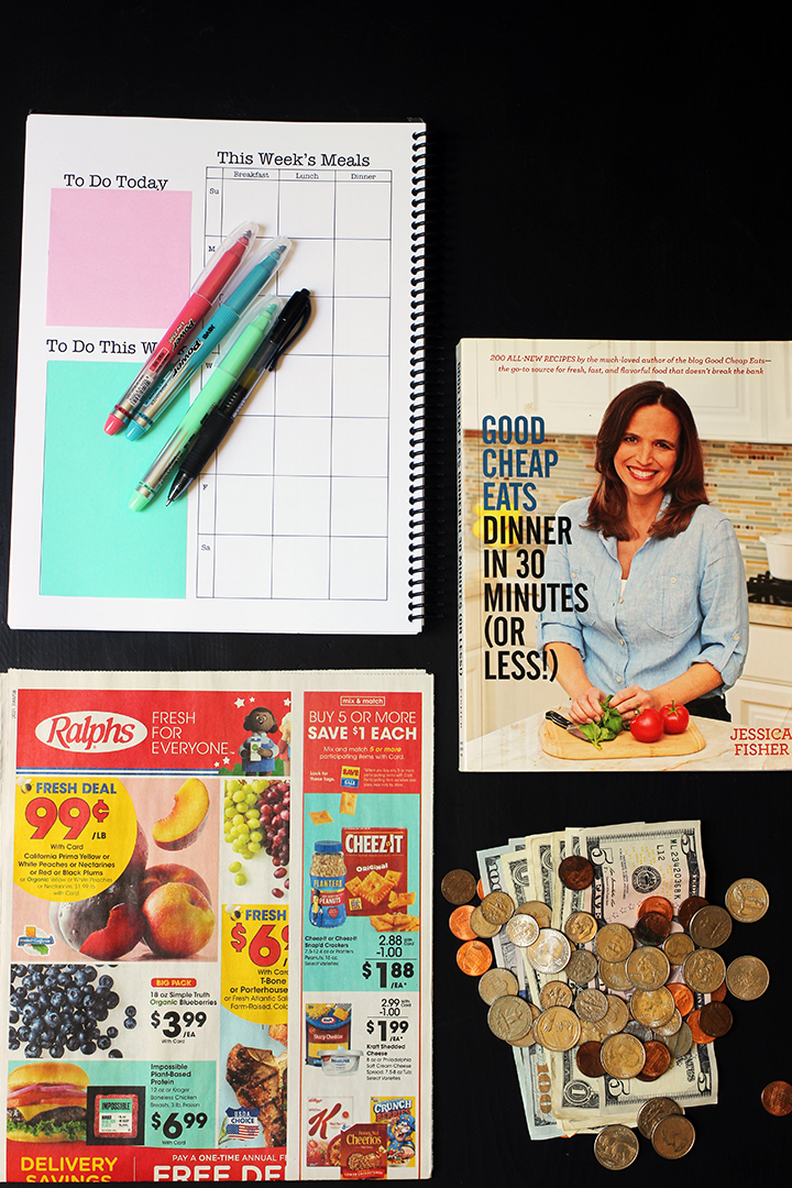 planner on table next to cookbook, pile of money, and grocery ad