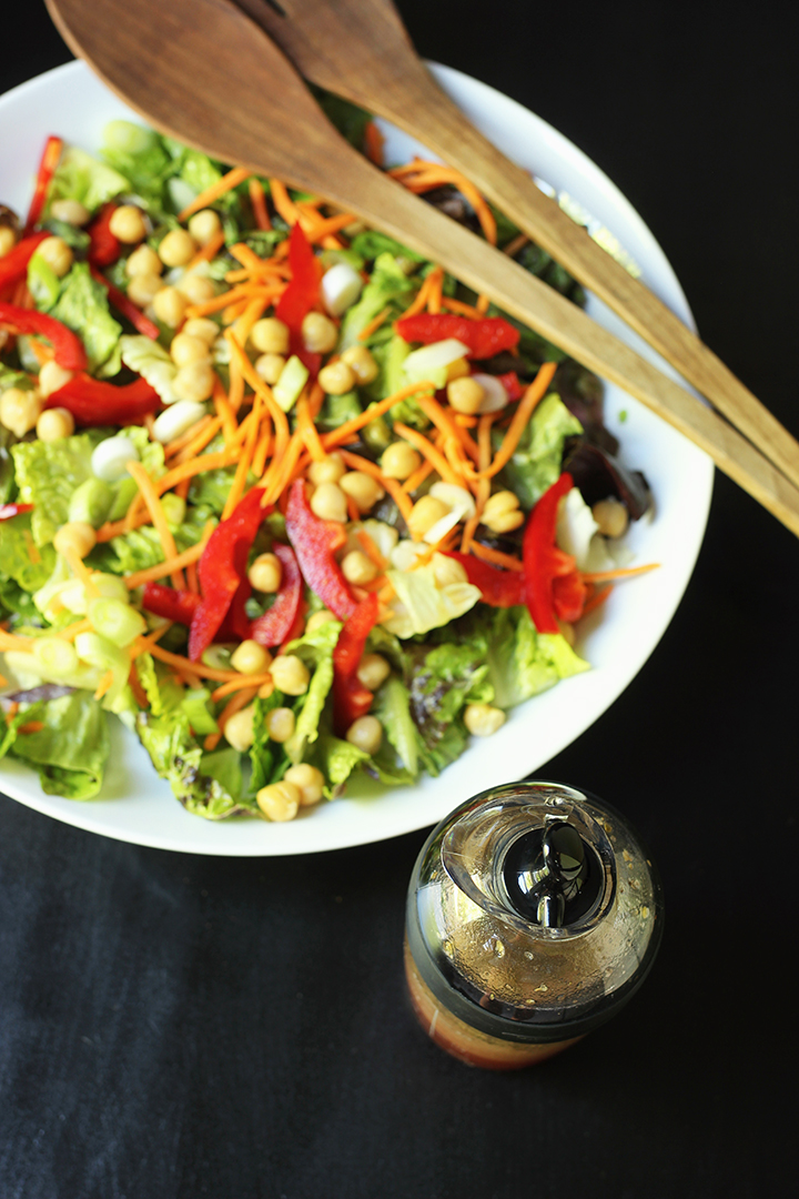 green salad in white bowl next to dressing cruet