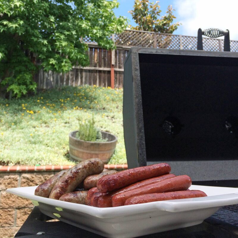 brats and hot dogs on platter next to open grill in backyard.