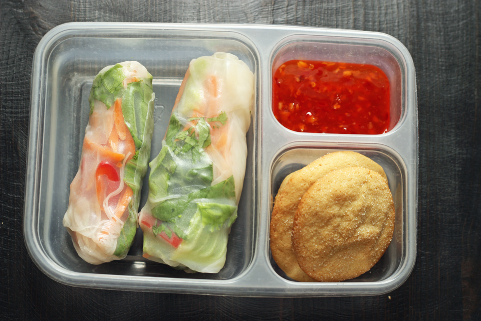 A plastic container with cookies and summer rolls