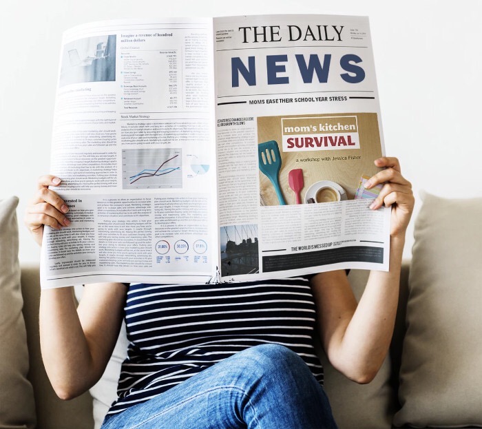 woman reading newspaper with ad for mom\'s kitchen survival workshop