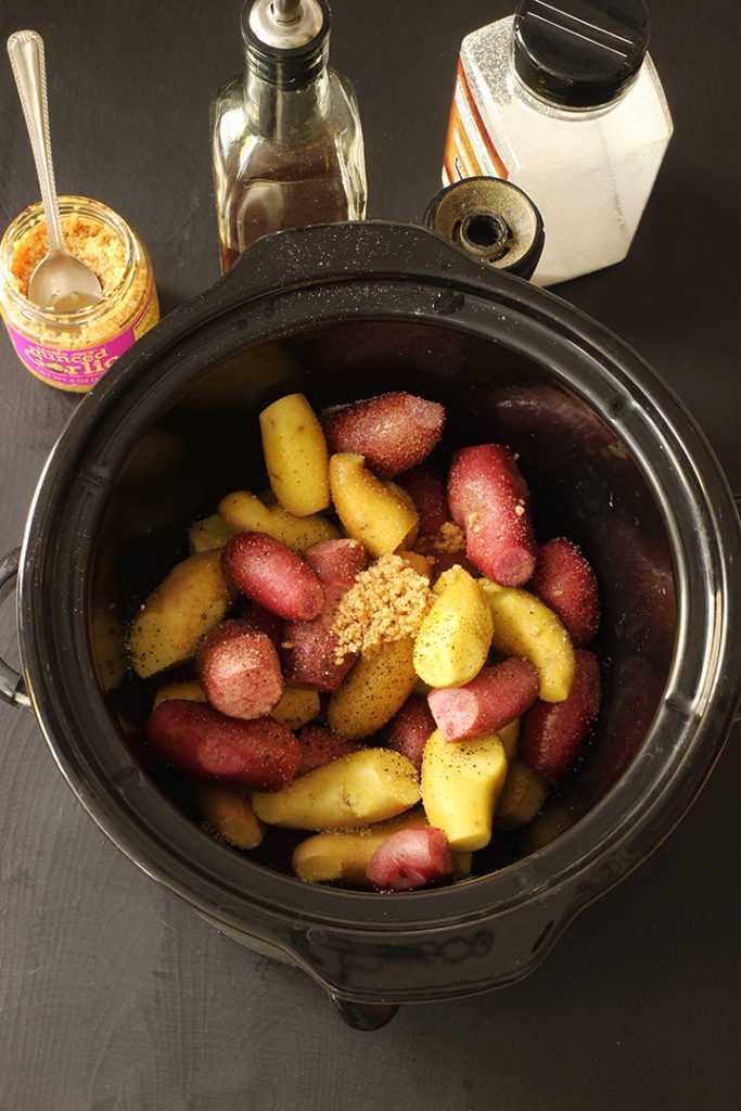 garlic and seasoning on potatoes in crock with ingredients nearby