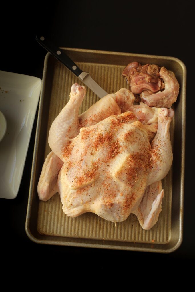 whole chicken with butter pats under the skin with knife and giblets nearby.