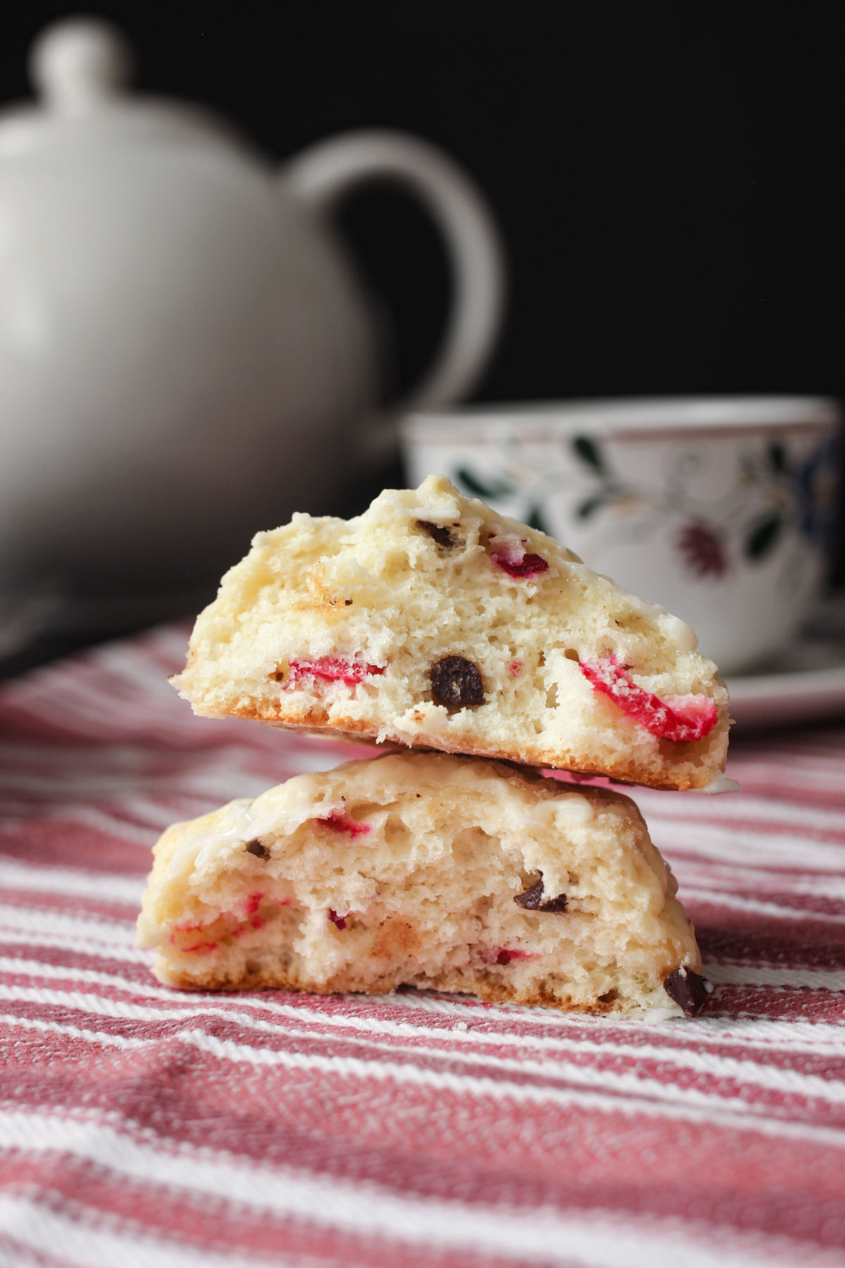 two halves of a scone stacked on a red striped cloth with a tea cup and tea pot in the background.