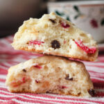 two halves of a cranberry chocolate chip scone stacked on each other on a red striped cloth.