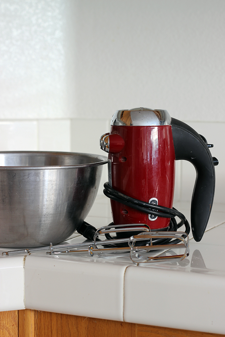 red hand mixer and beaters next to stainless bowl on counter