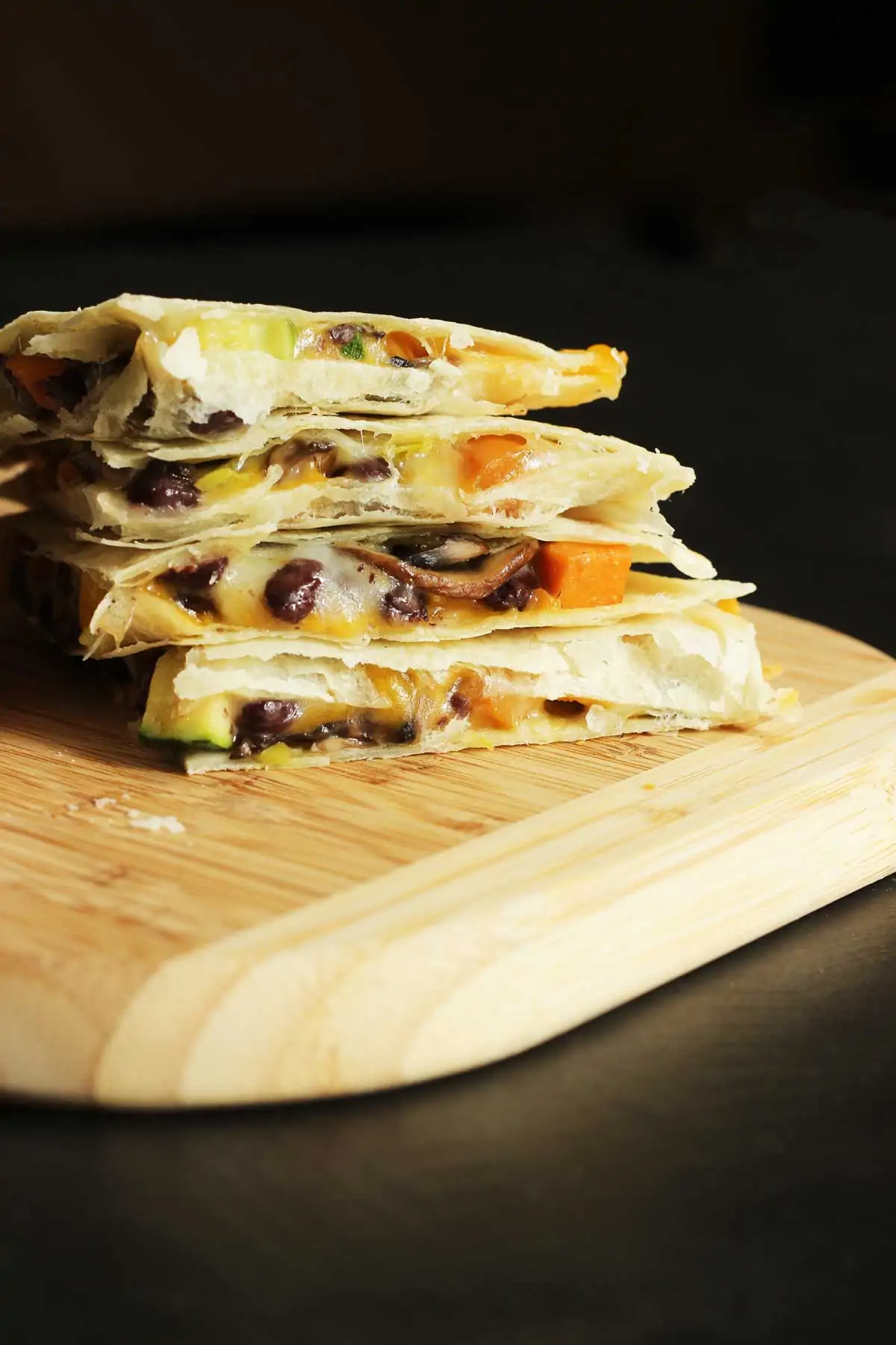 quarters of quesadilla stacked on wooden cutting board.
