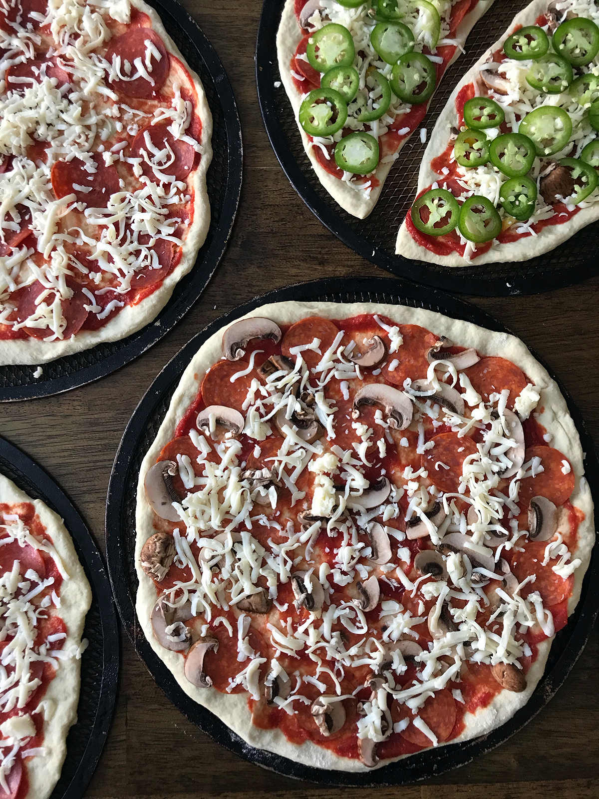 unbaked pizzas on screens on table