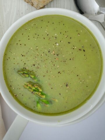 square overhead crop of asparagus soup in white bowl.