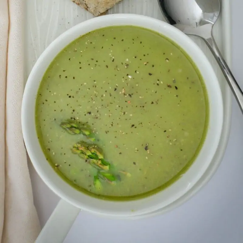 square overhead crop of asparagus soup in white bowl.