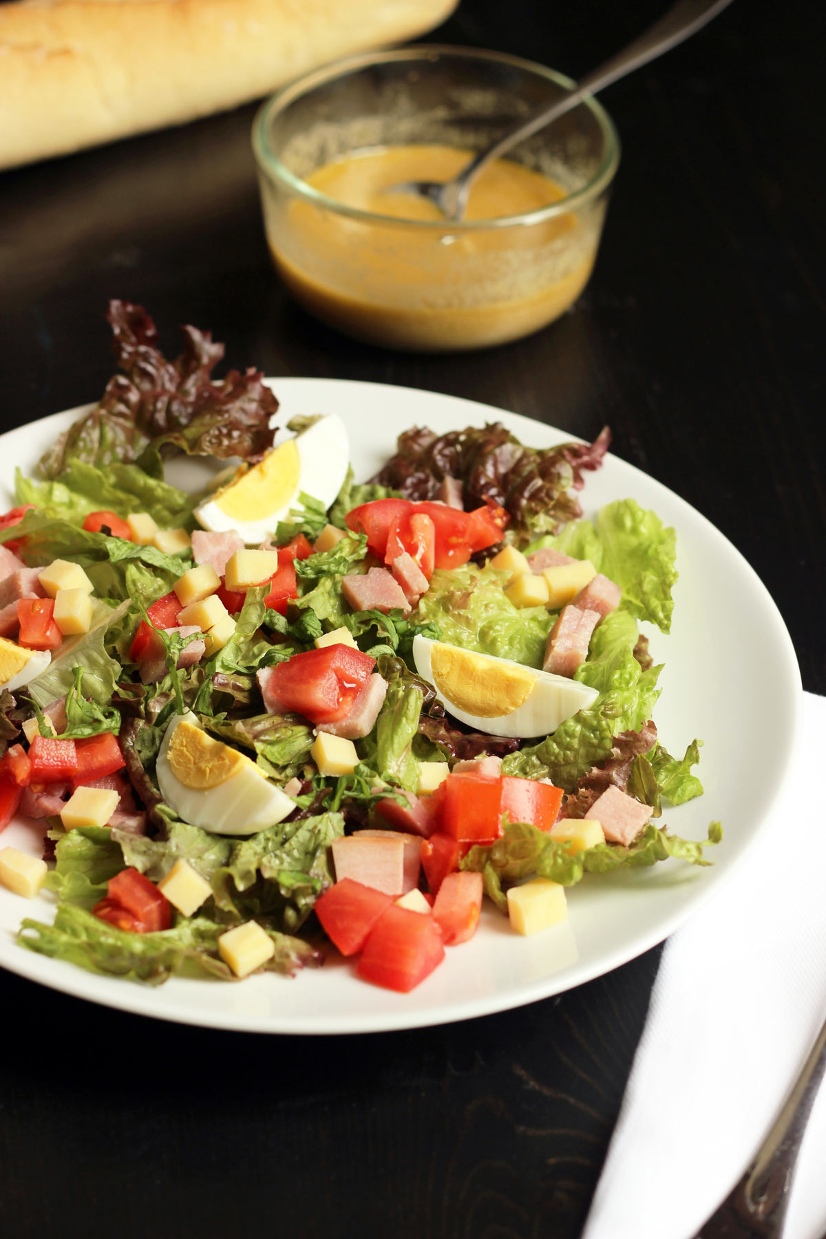 ham and gruyere salad with egg on a white plate with a dish of vinaigrette nearby.