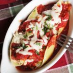 gratin dish with shell pasta stuffed with chicken and cream cheese topped with sauce and cheese.