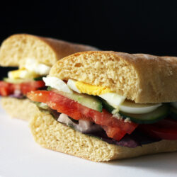 egg sandwich with vegetables cut in half on a white board.