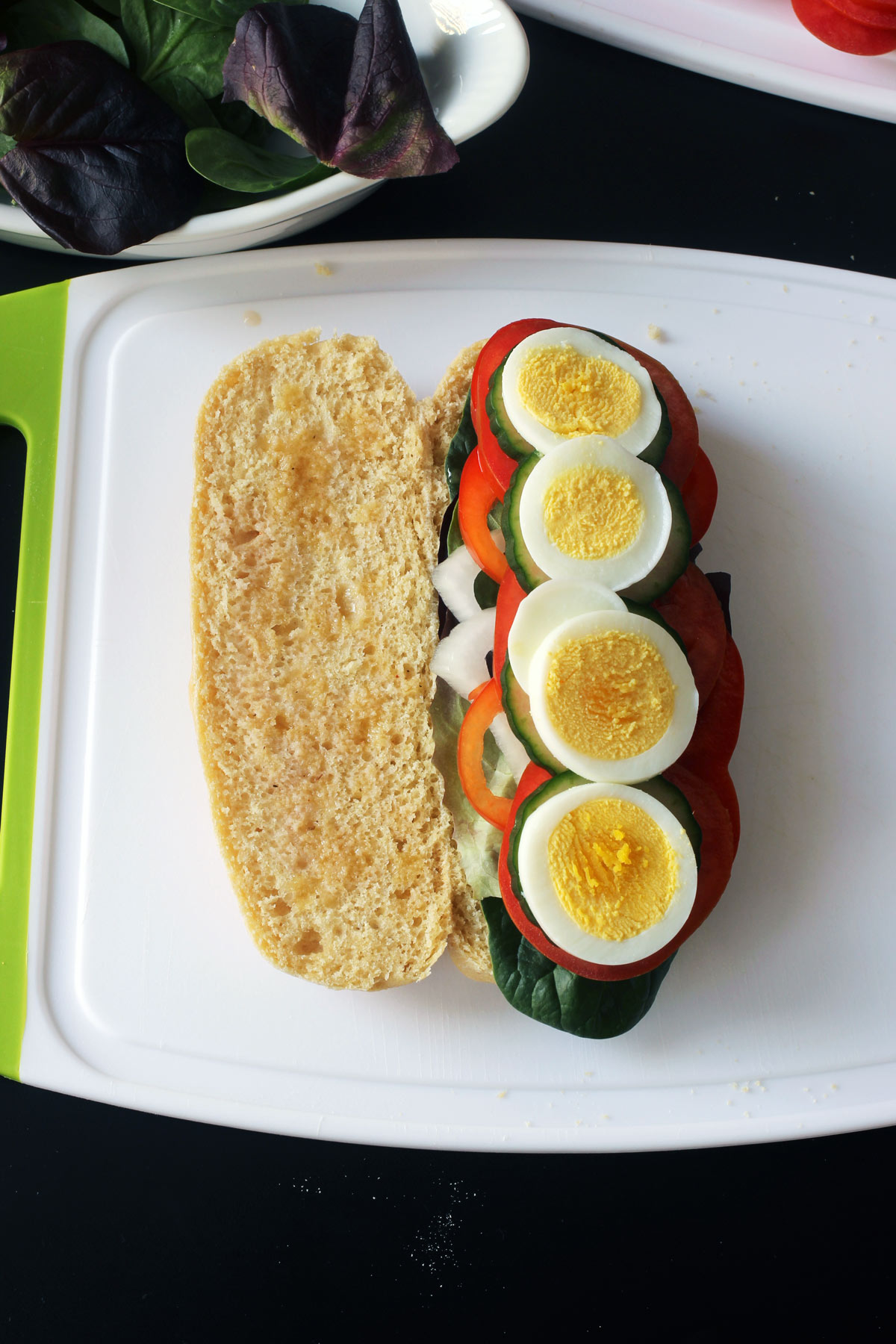 sandwich open with sliced hard boiled egg on one side atop vegetables.