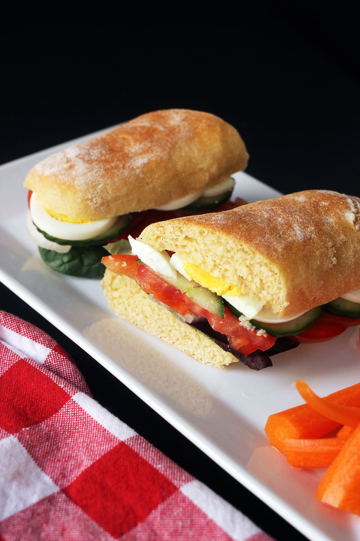 egg sandwich cut in half on platter with carrots