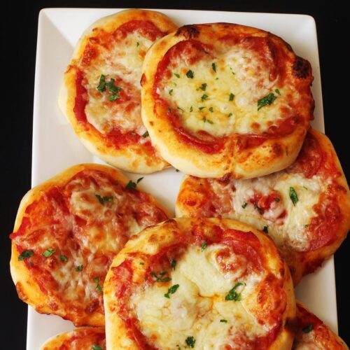 mini pizzas on a white rectangular tray on a black table.