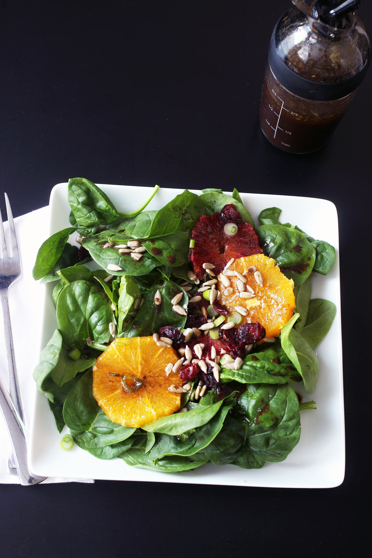 spinach salad on square plate next to cruet of dressing