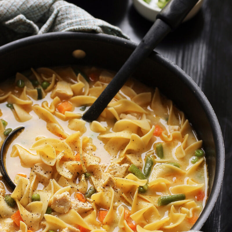 creamy chicken noodle soup in a large black pot with black ladle.