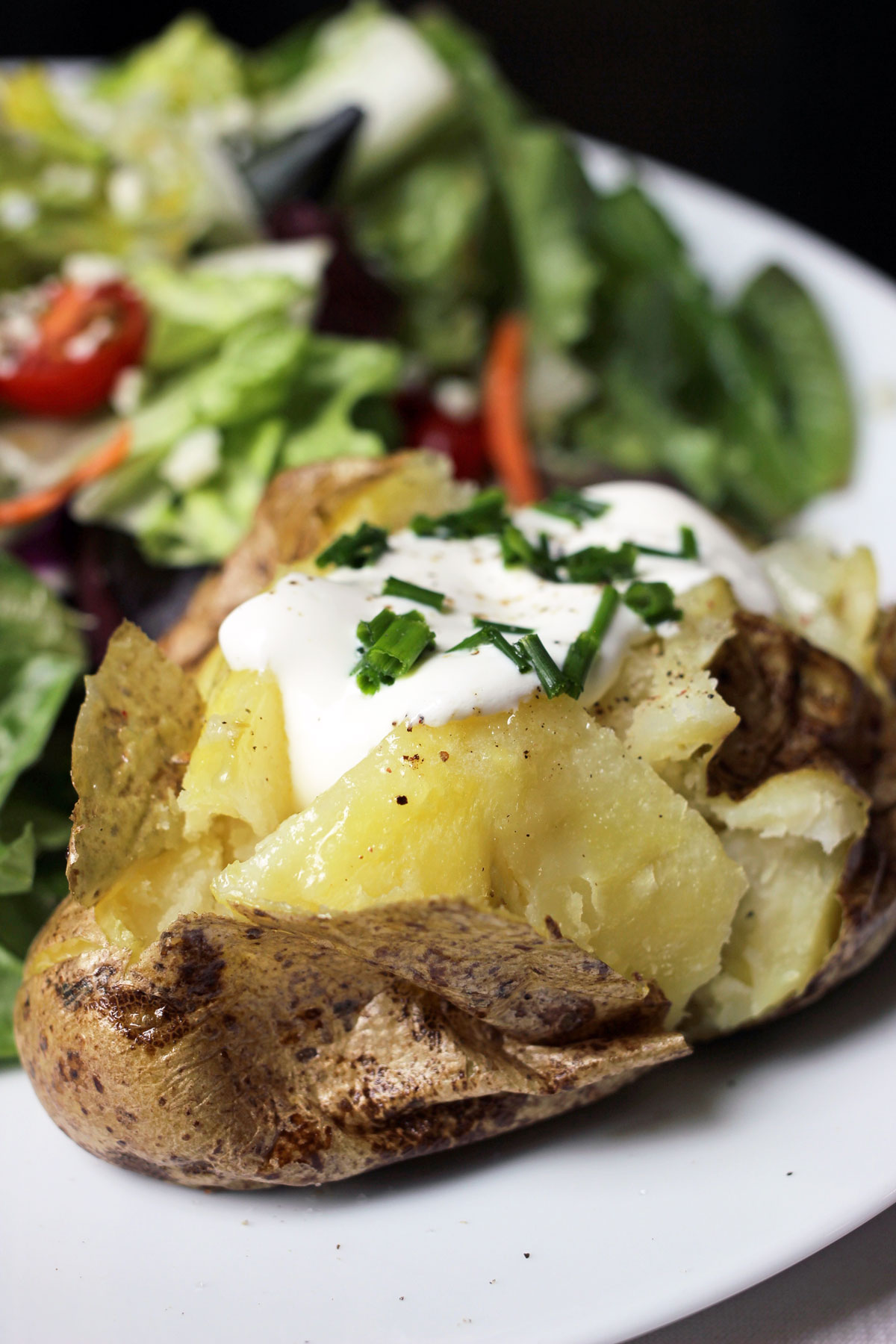 baked potato with sour cream on plate with salad