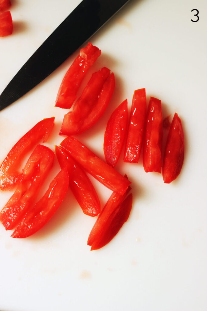 slices of tomato that have been cut into strips on white cutting board.