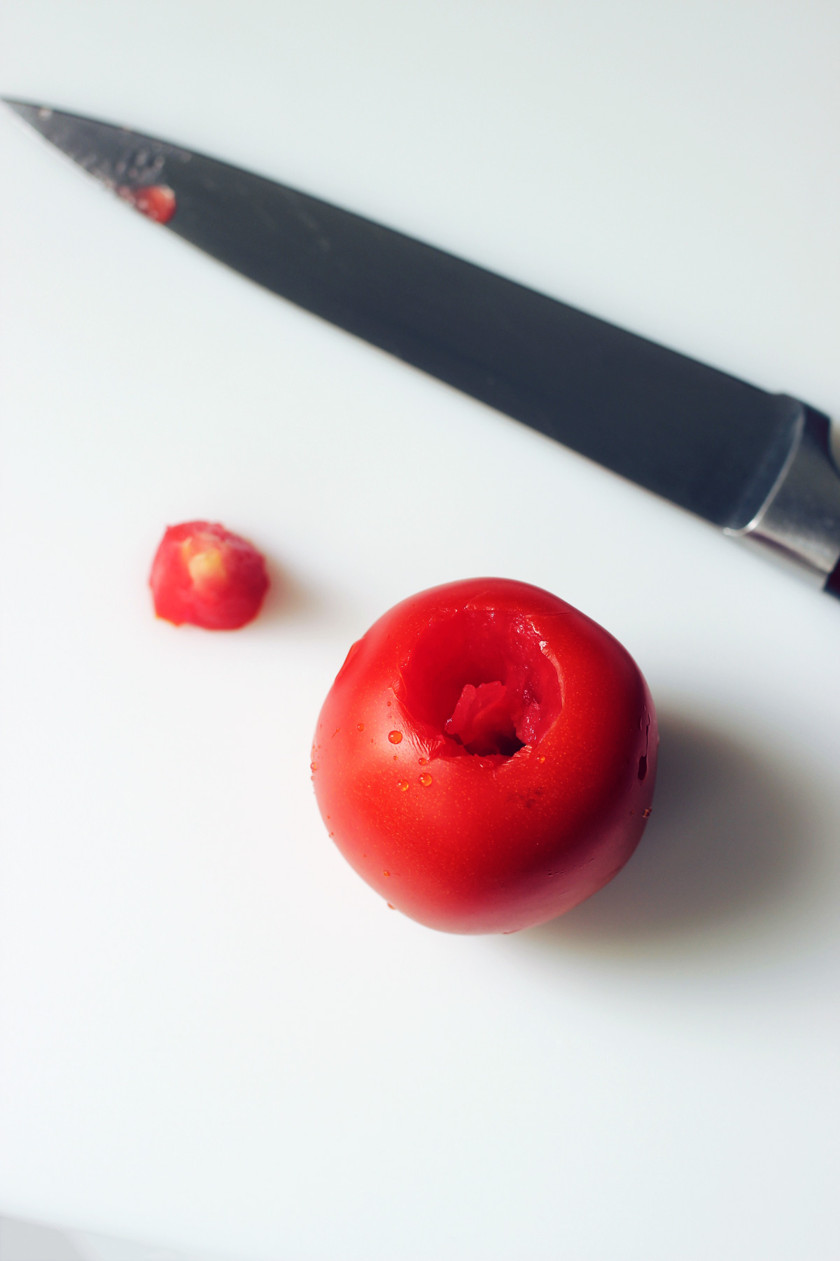 cored tomato on white cutting board with knife and core