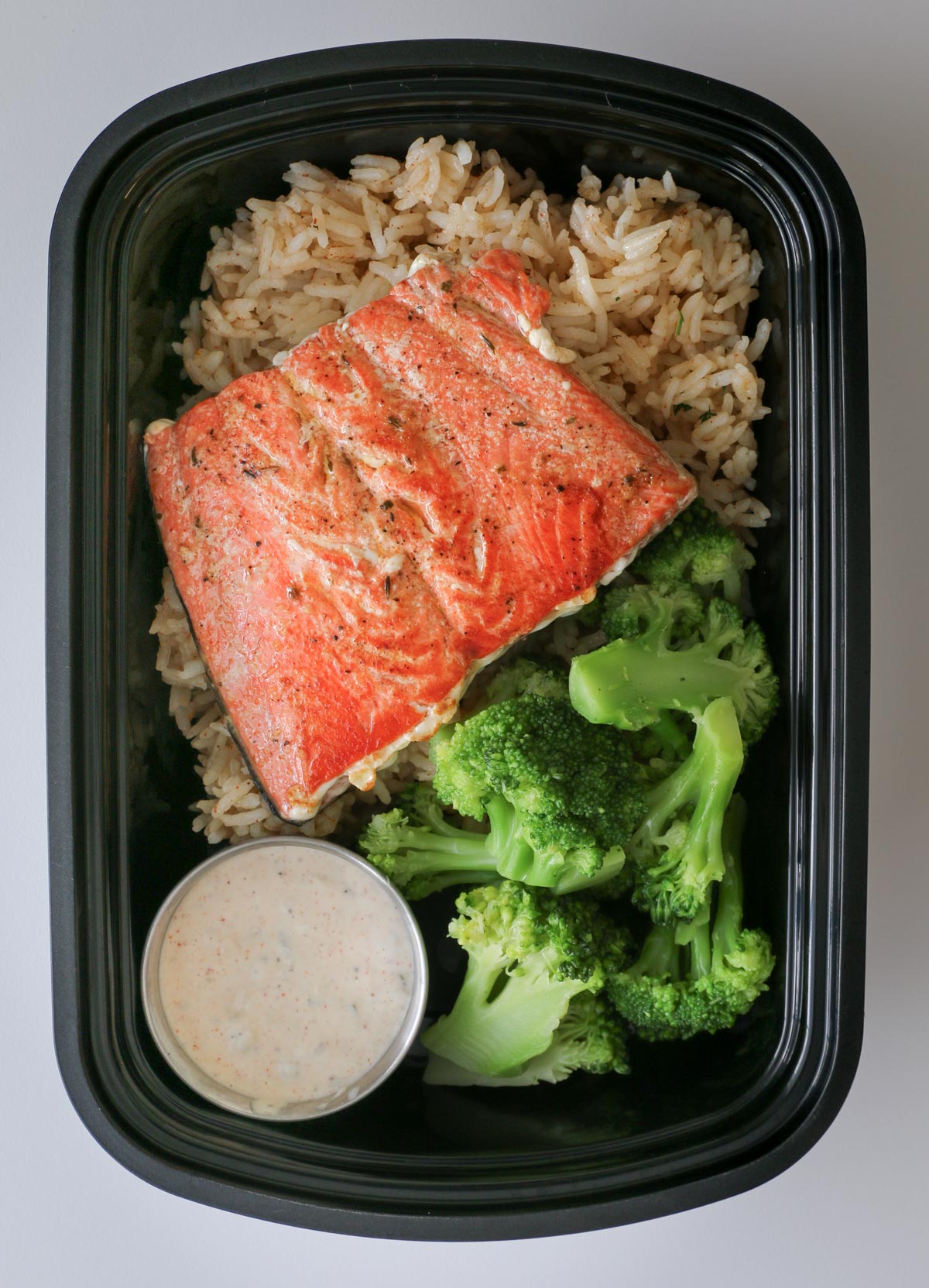 meal prepped salmon box with rice, broccoli, salmon fillet, and tartar sauce.