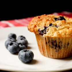 blueberries on white plate next to blueberry muffin.