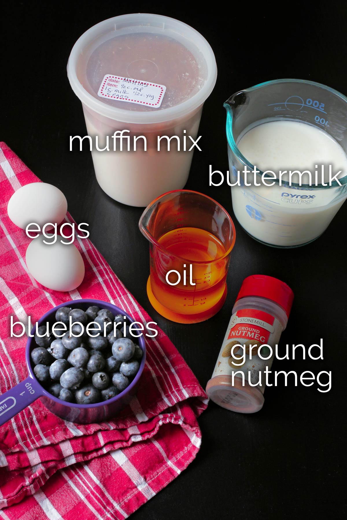 ingredients for blueberry muffins laid out on table on red cloth.