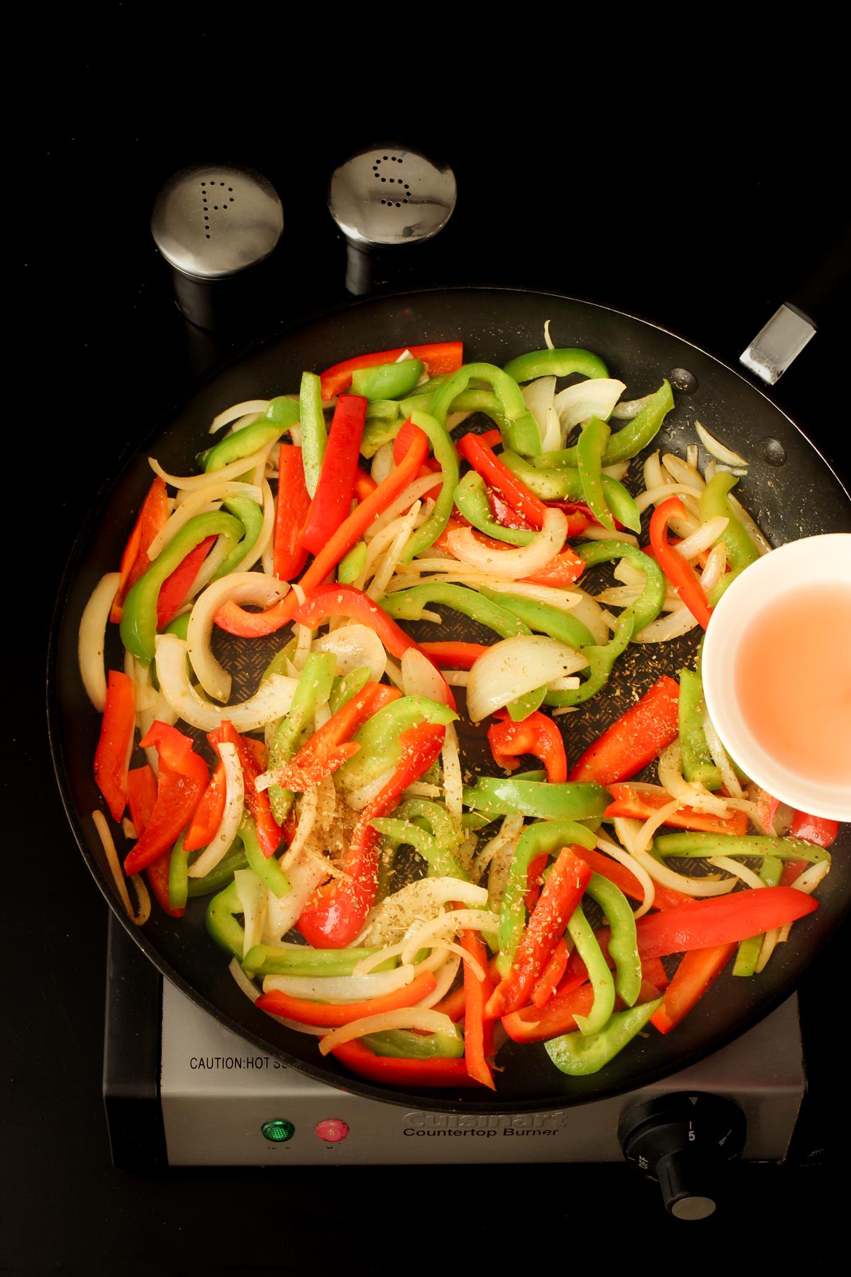 adding salt, pepper, vinegar, and oregano to the vegetables in the skillet.