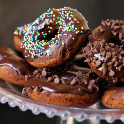 stack of chocolate baked donuts on beaded glass cake platter.