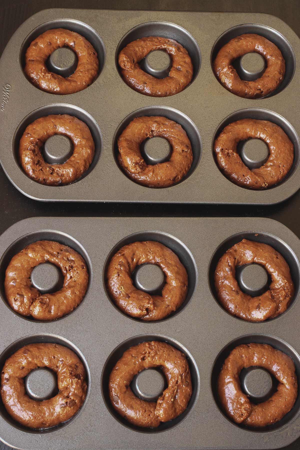 two donut pans filled with chocolate donut batter.