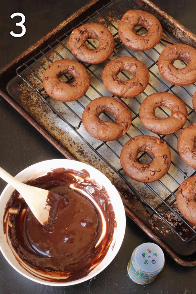 the donuts on a wire rack sitting inside a sheet pan next to the bowl of glaze.