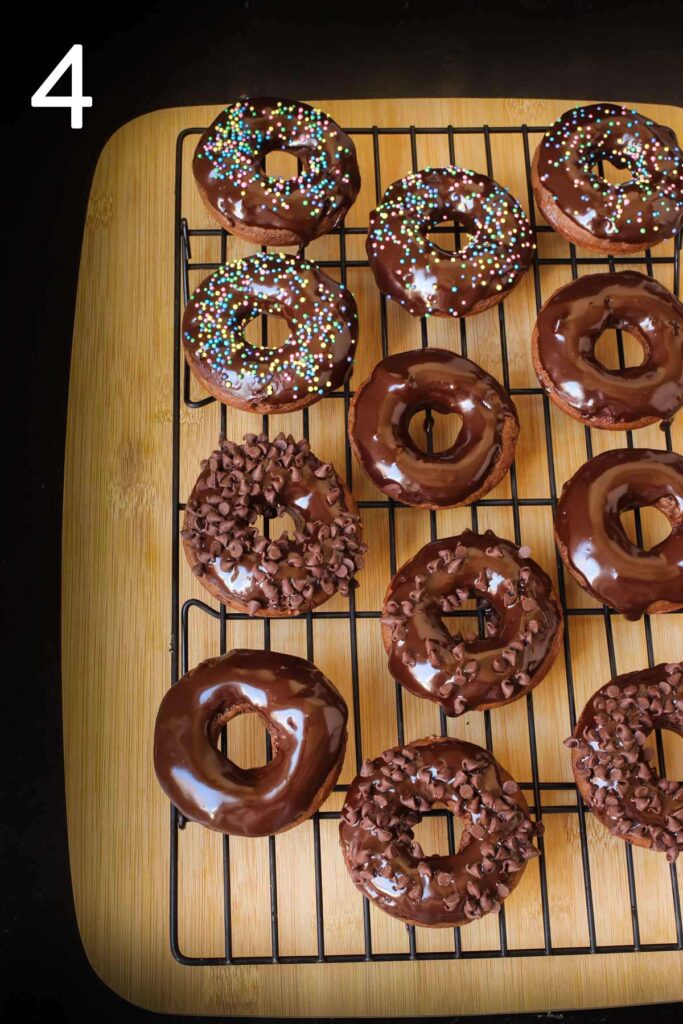 glazed chocolate donuts with sprinkles and chocolate chips cooling on rack over a wooden board.