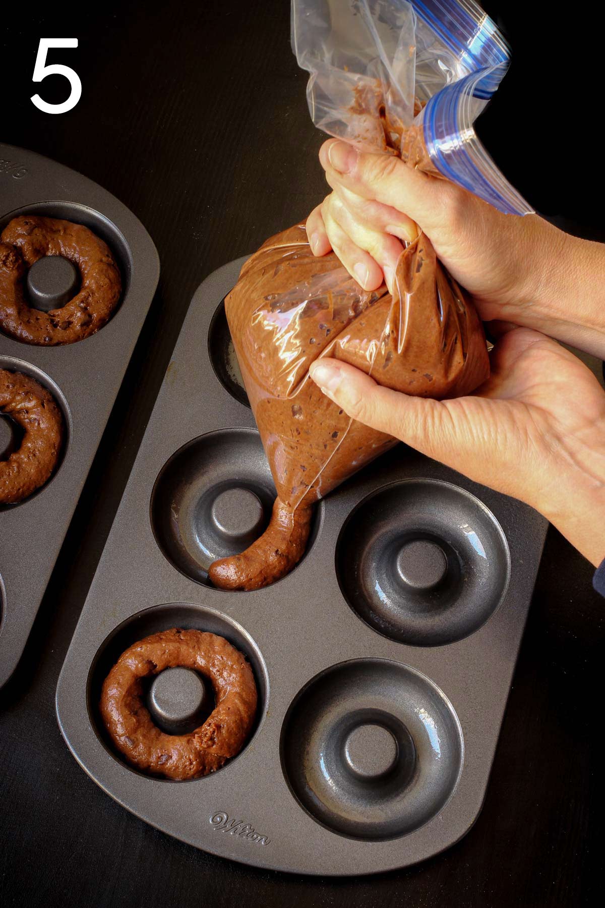 piping chocolate donut batter into greased donut pans.