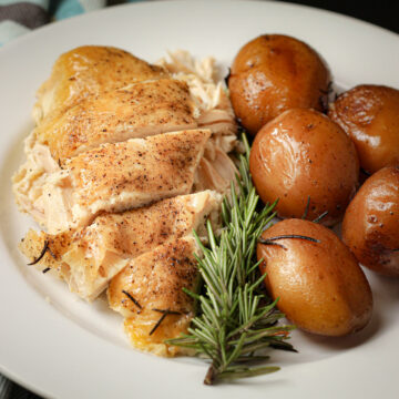 dinner plate with crockpot chicken breast and new potatoes with sprig of rosemary.